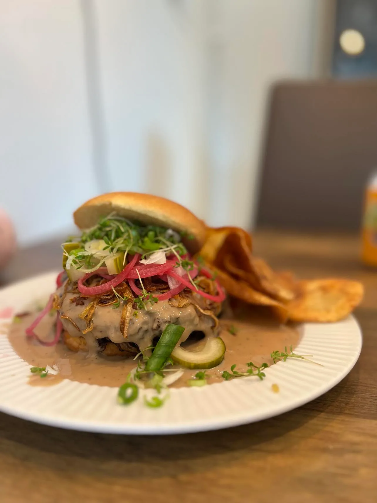 Gourmet burger with pickles and chips on plate.