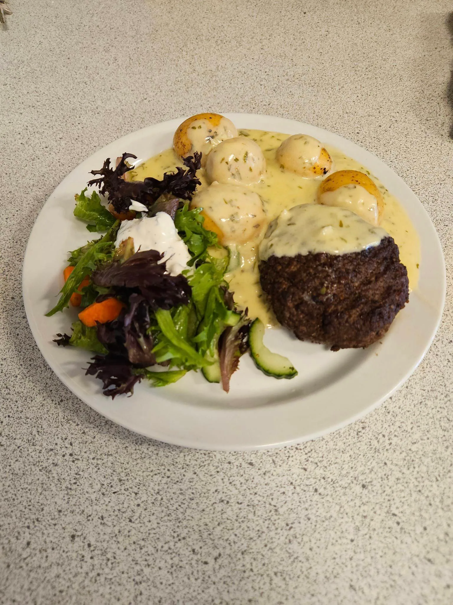 Plate of meat, potatoes, salad with dressing.