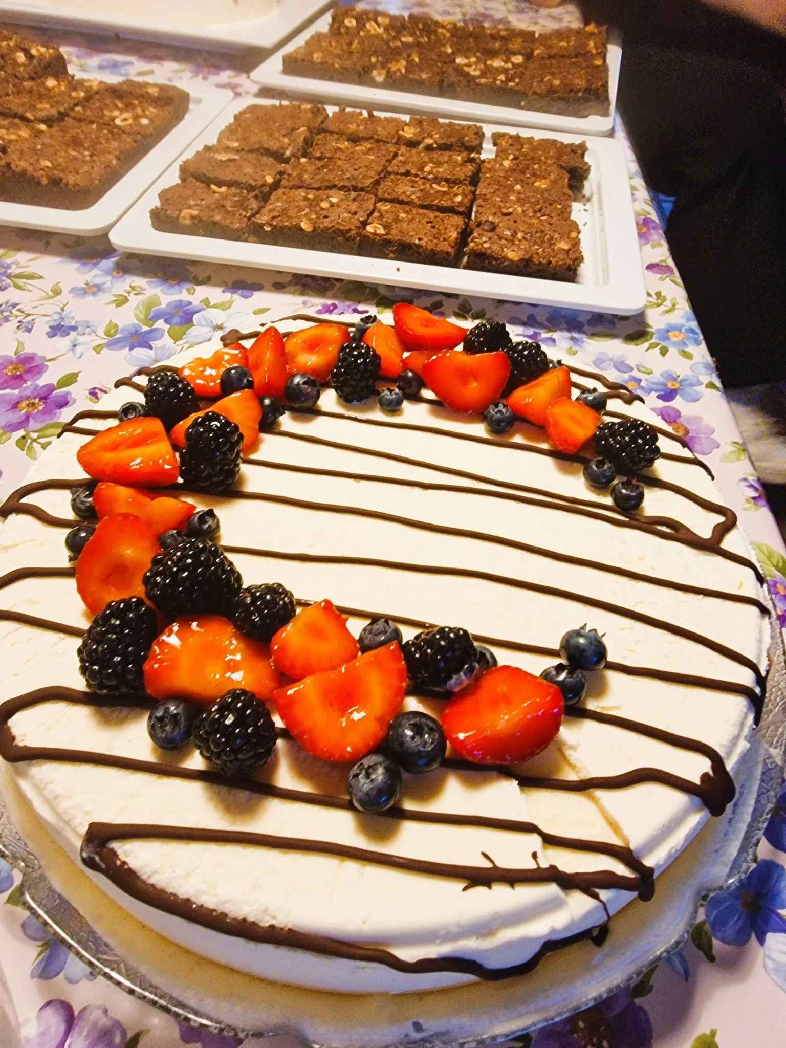Cheesecake with berries and chocolate drizzle on table.